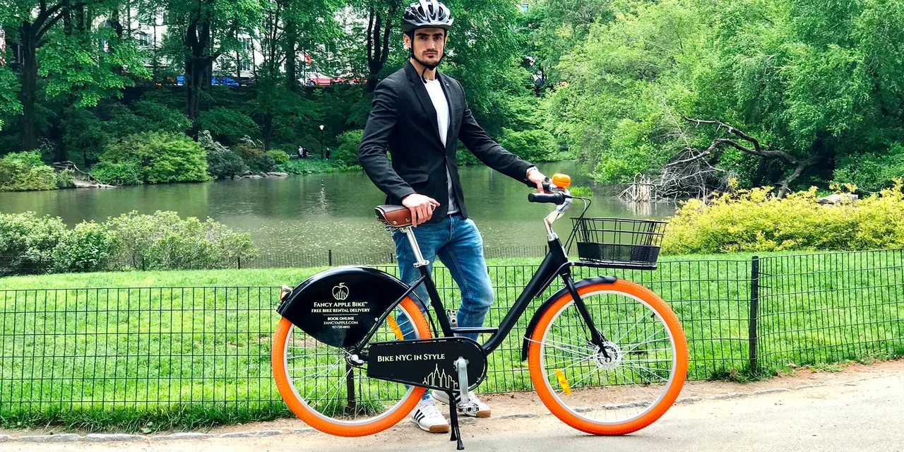 Rider standing with a black rental bike beside a Central Park pond